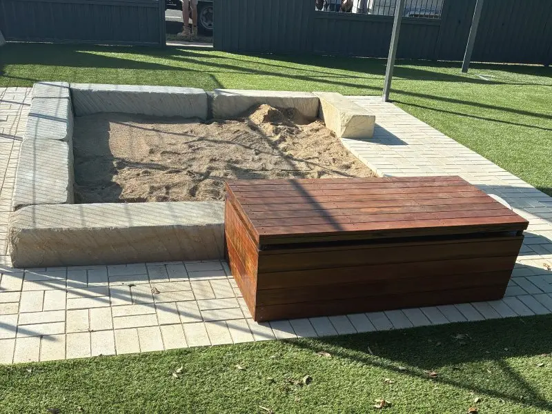 Sandstone block sandpit with a timber storage bench on synthetic turf