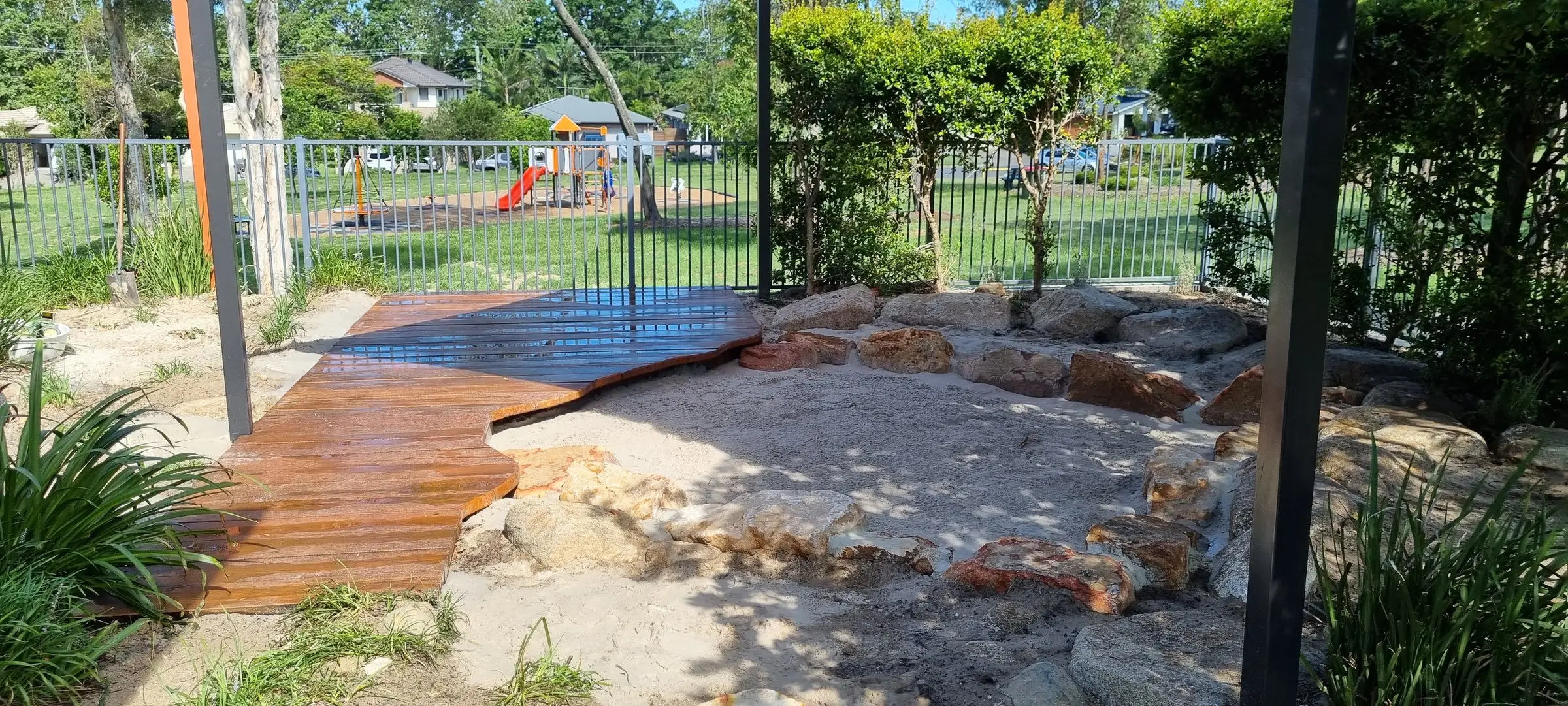 New timber deck, sandstone boulders and sand play area in a childcare nature play yard