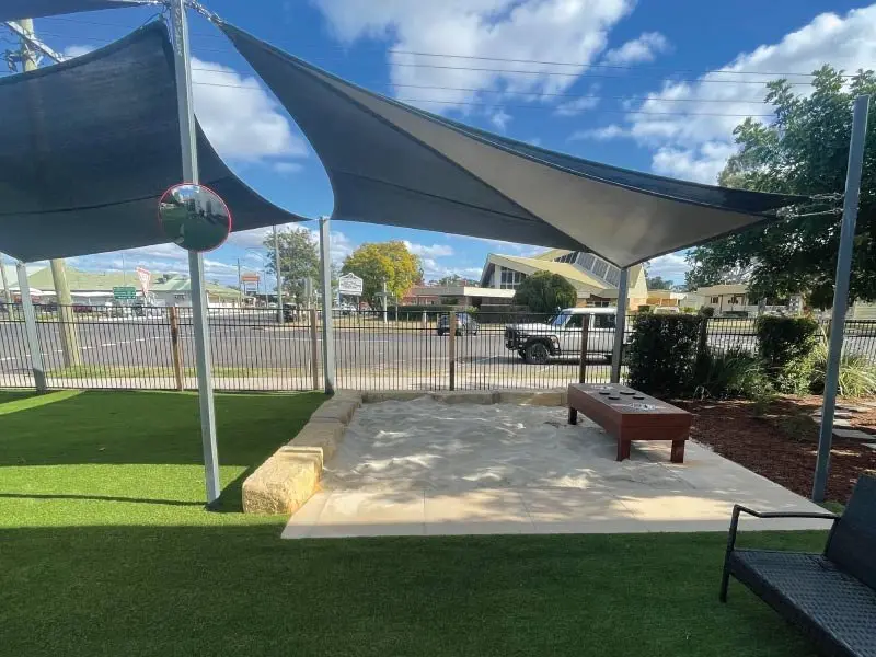 Shade sail over the new sandpit with the street beyond the fence