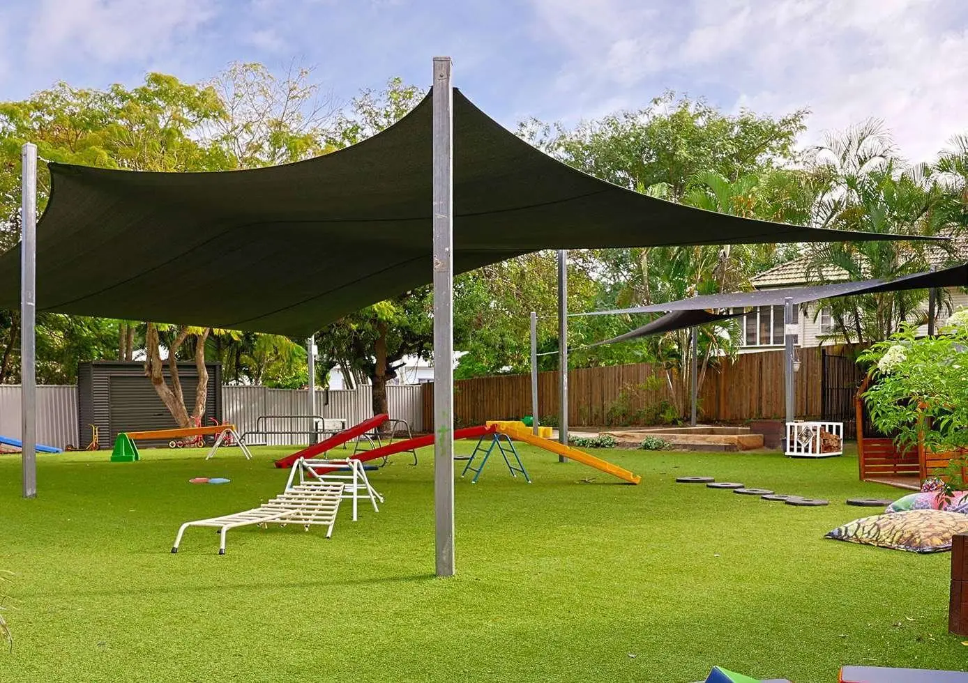 Shade sails over a synthetic grass yard with timber play equipment at a childcare centre